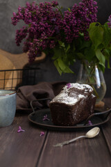 Chocolate cake on a wooden with a cup of tea and lilacs.