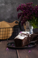 Chocolate cake on a wooden with a cup of tea and lilacs.