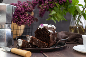 Chocolate cake on a wooden with a cup of tea and lilacs.