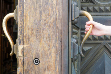  A small childish or girlish hand is held by the door handle of a large and thick door.