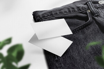 Clean minimal business card mockup floating on black jeans and plant
