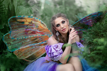 A beautiful woman is a little cute fairy with butterfly wings in a green exotic forest. Fantasy...