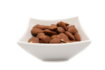 A white bowl with almonds, isolated on white background. The almond is the fruit of the almond tree (Prunus dulcis). It has a cinnamon-colored film that surrounds it as well as an outer shell.