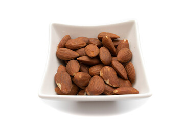 A white bowl with almonds, isolated on white background. The almond is the fruit of the almond tree (Prunus dulcis). It has a cinnamon-colored film that surrounds it as well as an outer shell.
