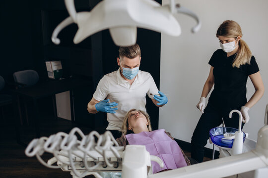 The girl is at the reception at the dentist. A happy client at the dentist smiles and shows with his hand that everything is okay. Dental bleaching. Dental clinic. Treatment of teeth in a modern clini