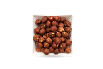 A white bowl with hazelnuts, isolated on white background.Hazelnut is the nut-like fruit of the common hazel, Corylus avellana. Etymologically it comes from the Latin nux abellana.