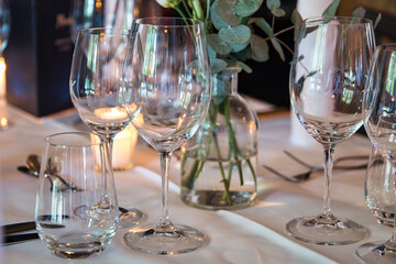 The table in a restaurant is decorated for a wedding dinner, with small candles and flowers and plentiful reflections in the wine and water glasses. 