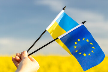 Flags of Ukraine and the European Union held in a woman's hand against the background of the sky...