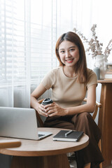 Confident and attractive Asian business woman sitting at a table by the window work on a laptop computer