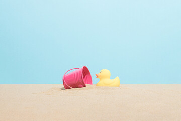 Yellow rubber ducky and pink bucket on the beach sand. Minimal summer vacation composition. © lagano