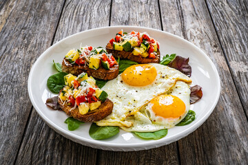 Sunny side up eggs, bruschetta and fresh vegetables on wooden table
