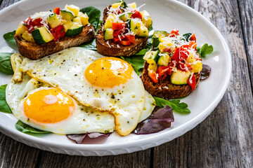 Sunny side up eggs, bruschetta and fresh vegetables on wooden table
