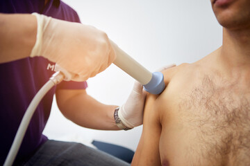 Shock wave therapy of the shoulder joint. Physiotherapist doctor uses medical equipment for highly...