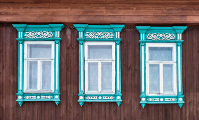 Three old windows with wooden turquoise architraves with patterns on brown board wall. - obrazy, fototapety, plakaty