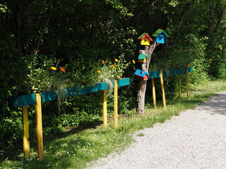 Gravel path. Vases with gerbera plants, colorful wooden flowerpots, birdhouses.