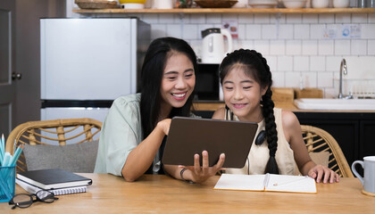 Mother and asian kid little girl learning and looking at laptop computer making homework studying with online education e-learning system.children video conference with teacher tutor at home