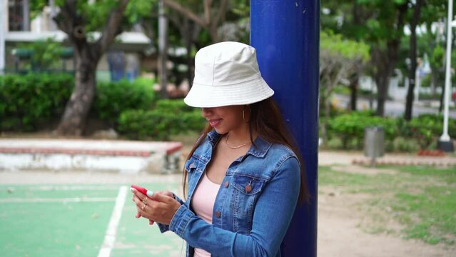 Latin woman with hat using cell phone on street