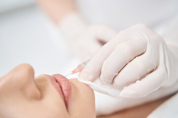 Obraz na płótnie Canvas Woman receiving lip injection in cosmetology clinic