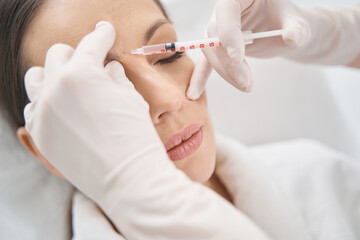 Beautician doing face lifting injection in woman forehead