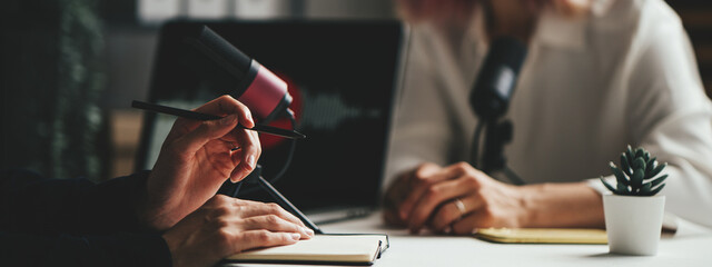 Two women host streaming audio podcast using microphone and laptop at home broadcast studio, hands close-up