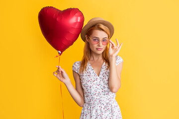 happy girl in glasses hold love heart balloon on yellow background