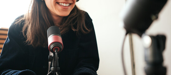 A woman host streaming her audio podcast using microphone at small broadcast studio, no face