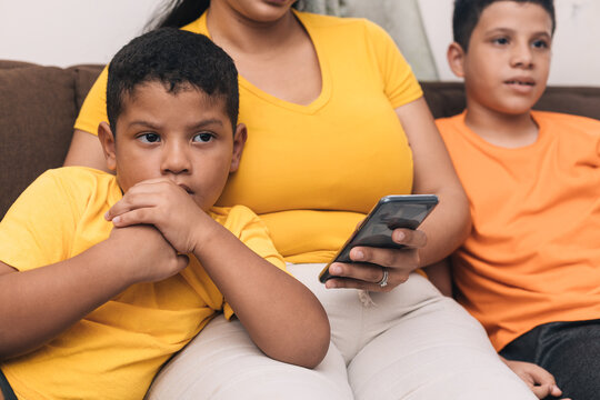 Mom Looking At The Cell Phone, Sitting With Her Two Children In The Armchair