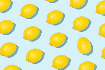Pattern made of bright yellow lemons in sunlight on blue background. Minimal styled summer concept.