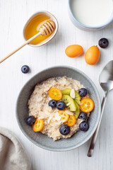 Oatmeal porridge with kumquat, blueberries, kiwi and almond flakes in a bowl.