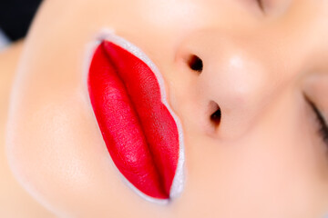 macro photography of the lips of a model prepared for a permanent makeup procedure with red applied...