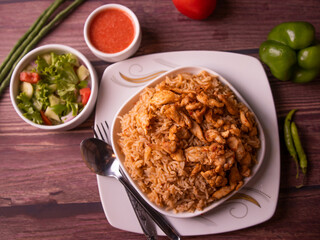 Spicy Indian chicken pulao with salad, sauce and spoon in a dish top view on wooden background pakistani chicken biryani