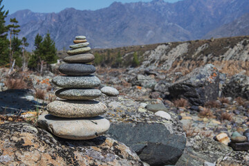 Pyramid of stones for meditation and making wishes on the bank of a mountain river against the backdrop of mountain peaks and forest.