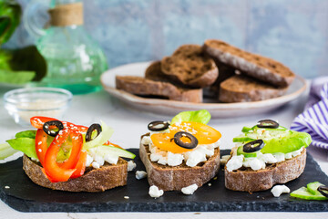 Appetizing bruschetta with feta cheese and vegetables on rye bread on a slate board. Close-up