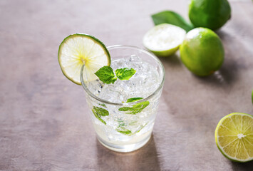 Refreshing mojito cocktail with mint and lime in a glass with ice on pink background with morning shadows. Concept summer citrus drink and fruits. Copy space