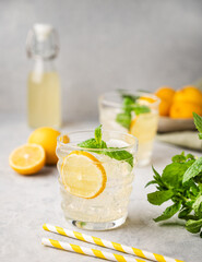 Lemonade soda drink with fresh lemons. Refreshing cocktail with lemon, mint and ice on textured light background. Summer cold drinks concept