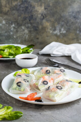 Spring rolls in rice paper made from shrimp, olives, lettuce and vegetables on a plate. Vertical