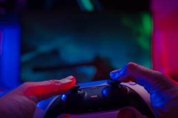 Close-up. The gamer holds a gamepad in his hands. Plays video games online with friends. Neon lighting. Technological background. Game strategy, cyberspace, esports.