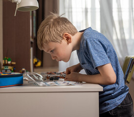 the boy is in his room at the table enthusiastically assembling a constructor