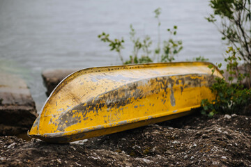 Photography, portrait of an old painted yellow inverted metal boat lying in nature near a lake,...