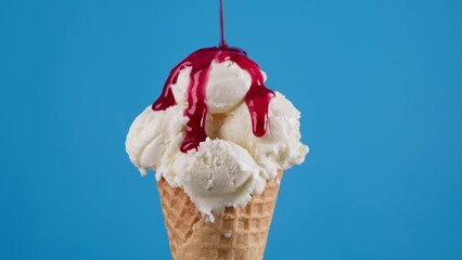 Strawberry topping flowing on white ice cream at blue background. Ice cream in cone with red sauce and colorful sprinkles. Food concept. Close-up in 4K, UHD