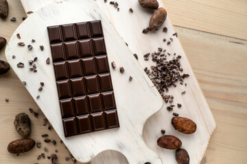 Dark bitter chocolate bar with cocoa beans on a wooden white background, top view. delicious chocolate. Space for text