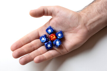 One dice with the symbol hammer and sickle surrounded by five blue cubes with the symbol usa star are on a man's palm. The concept of the ideology of communism and capitalism.