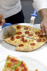 pizza artesanal de chorizo y queso fundido partiéndola en porciones el chef con cortador de pizza redondo