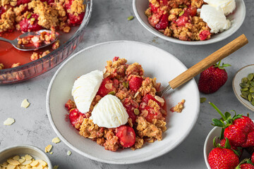 Strawberry crumble with ice cream and almonds in a plate with spoon on gray background. Tasty...