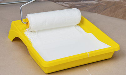 Painting apartment, renovating with white color paint. Paint roller in paint tray with white color in the tray on brown paper