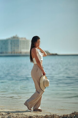 Young woman taking a barefoot walk on the beach enjoying the nice summer weather, wearing a hat. Vertical photo.