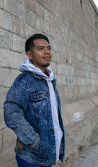 waist up shot of a guy with originarie mexican people features standing on a street with a concrete wall behind him