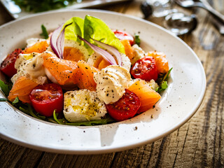 Salmon salad - smoked salmon hard boiled eggs, white cheese and green vegetables on wooden table
