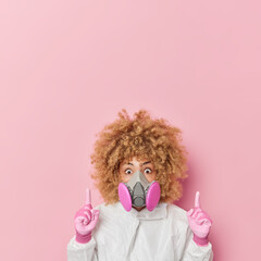 Impressed curly haired young woman in gas mask protective suit warns about danger tells about...