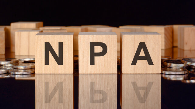 npa - text on wood blocks on black background with coins. front view. business concept